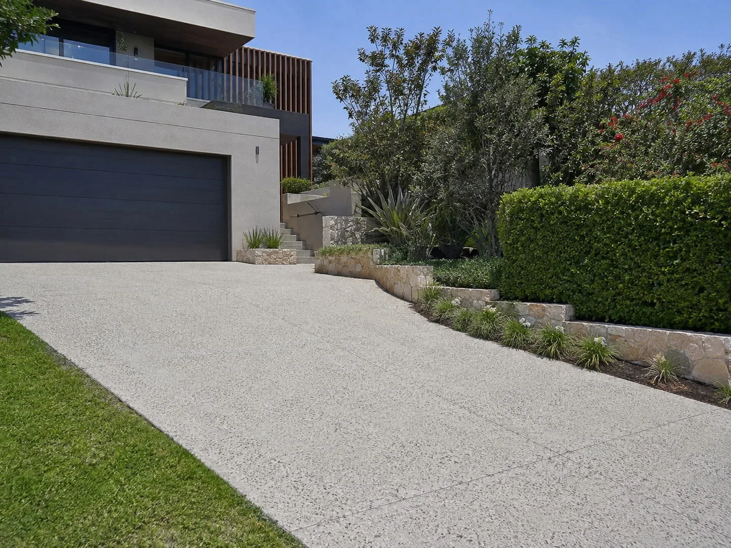 Resurfaced driveway running to a double garage beside a clipped hedge and sandstone retaining wall