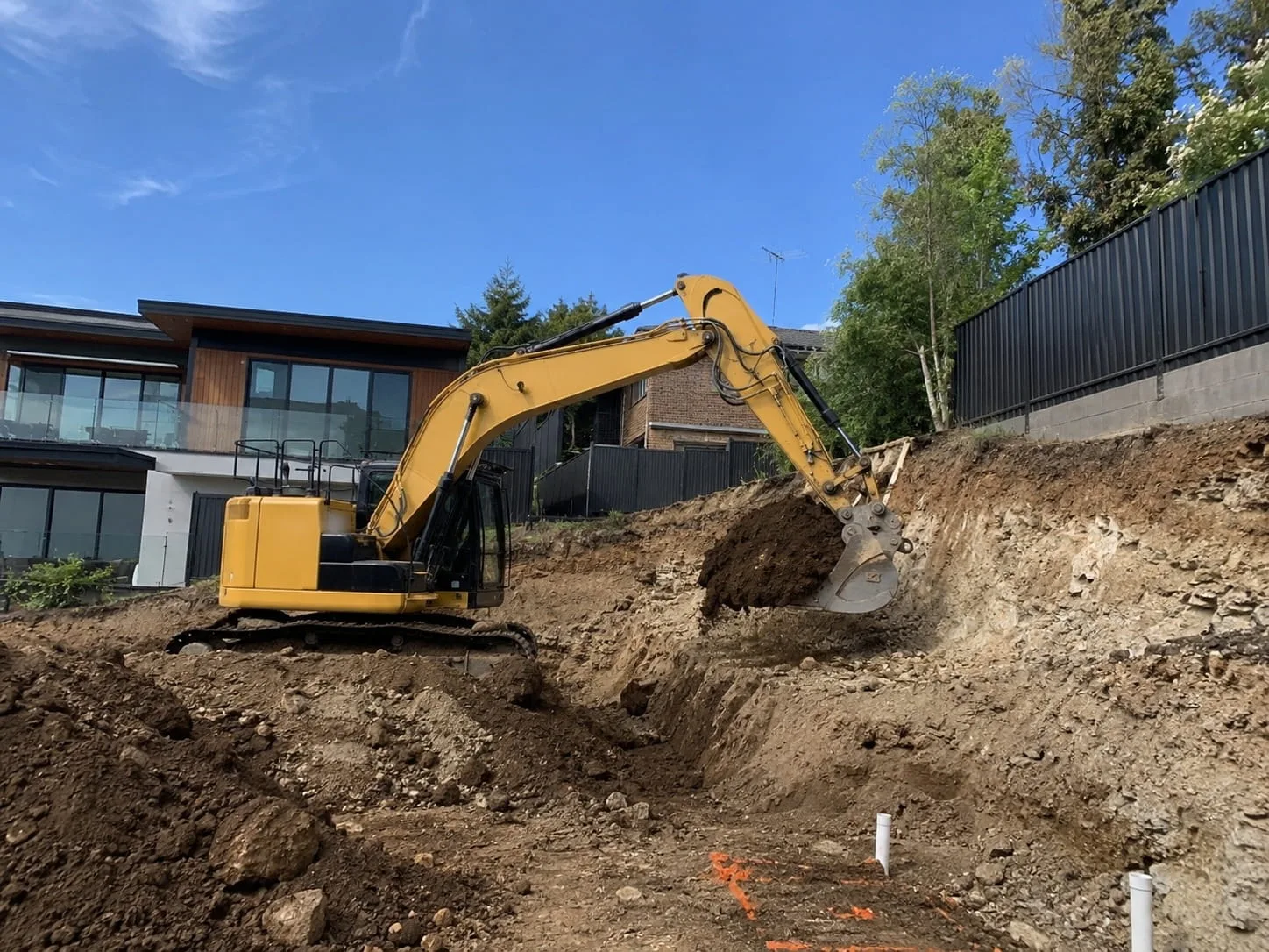 Excavator cutting into a batter beside a contemporary Newcastle home