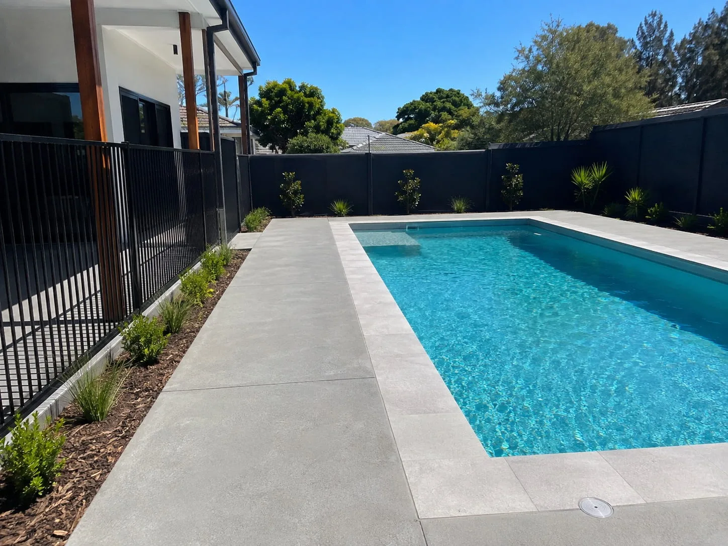 Pale concrete pool surround running the length of a swimming pool behind glass fencing at a Newcastle home