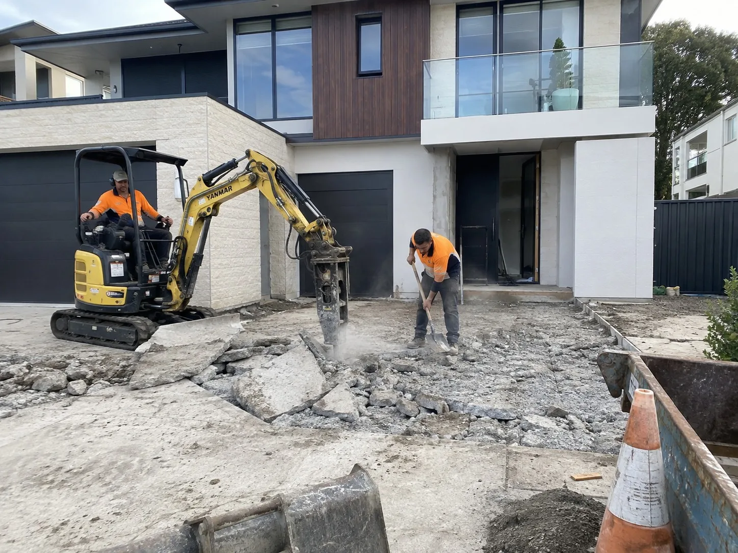 Mini excavator and a worker breaking up an old concrete driveway in front of a modern Newcastle home