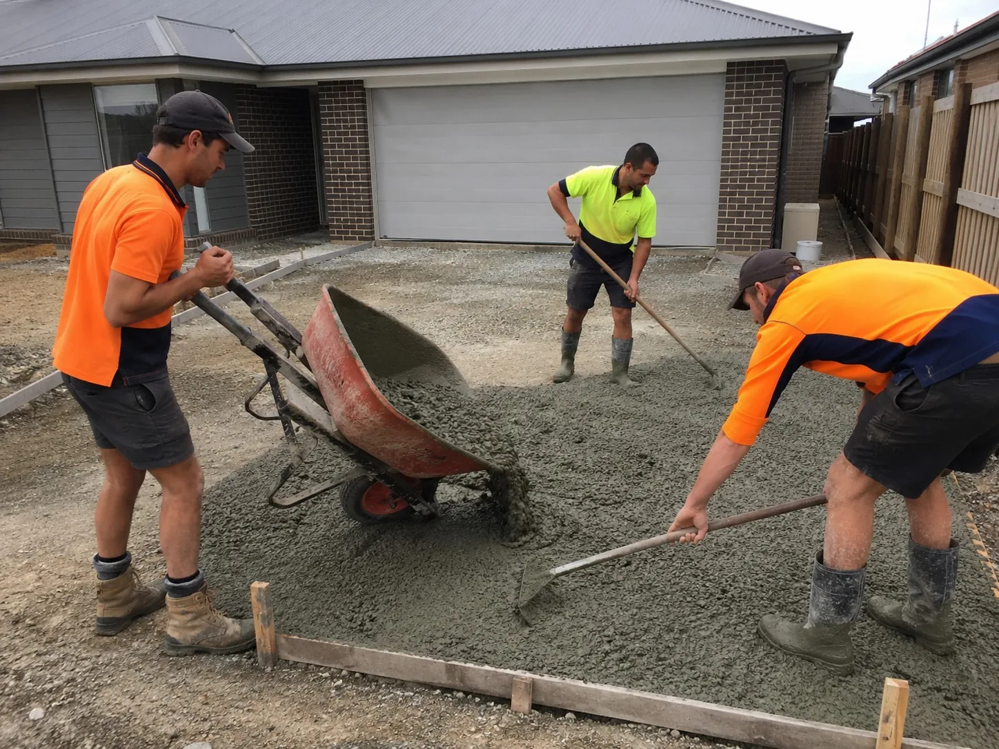 Three Newcastle concreters barrowing and raking fresh concrete into a driveway pour
