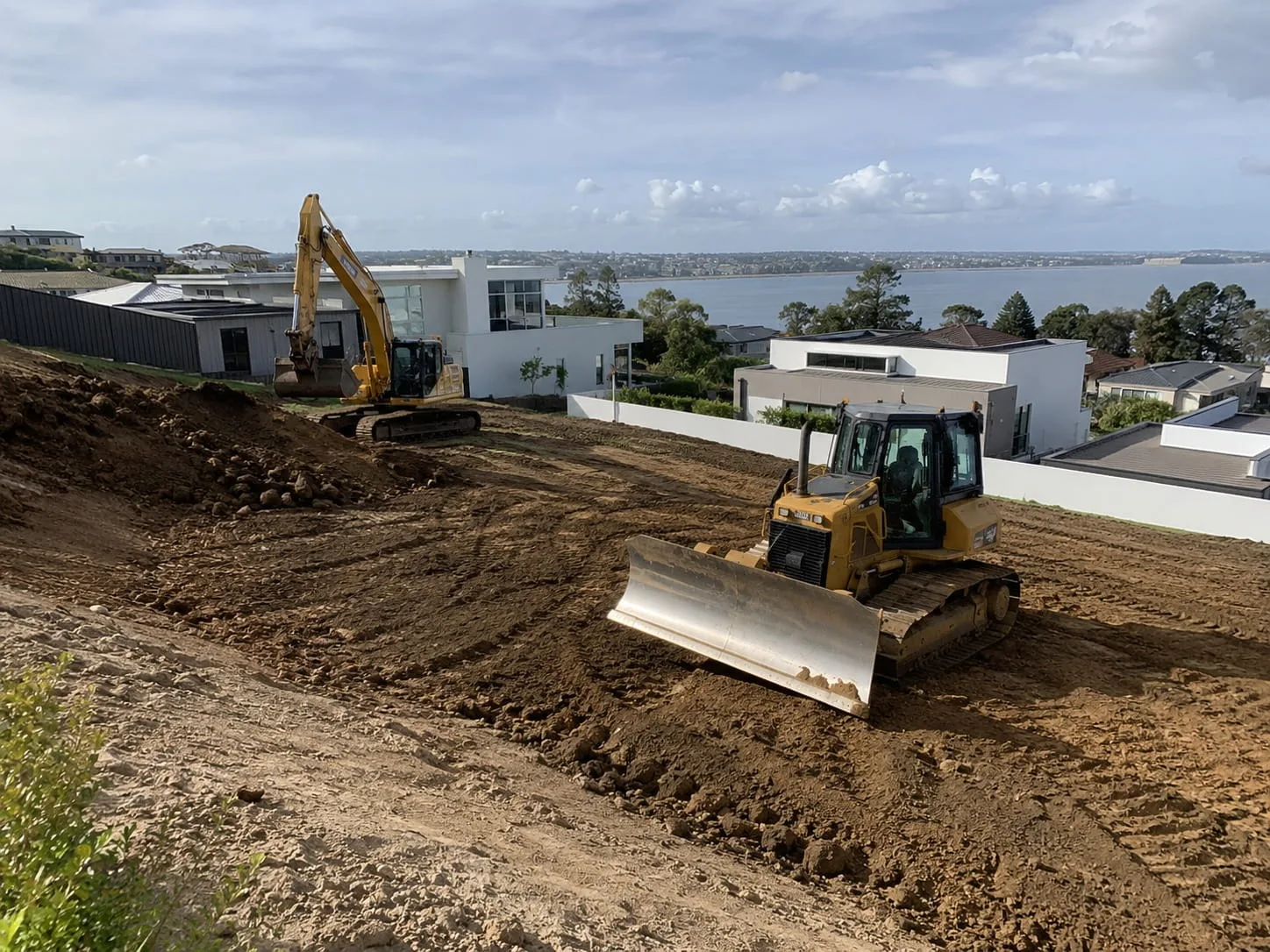 Dozer and excavator shaping a cut-and-fill building pad on a Newcastle block above the water