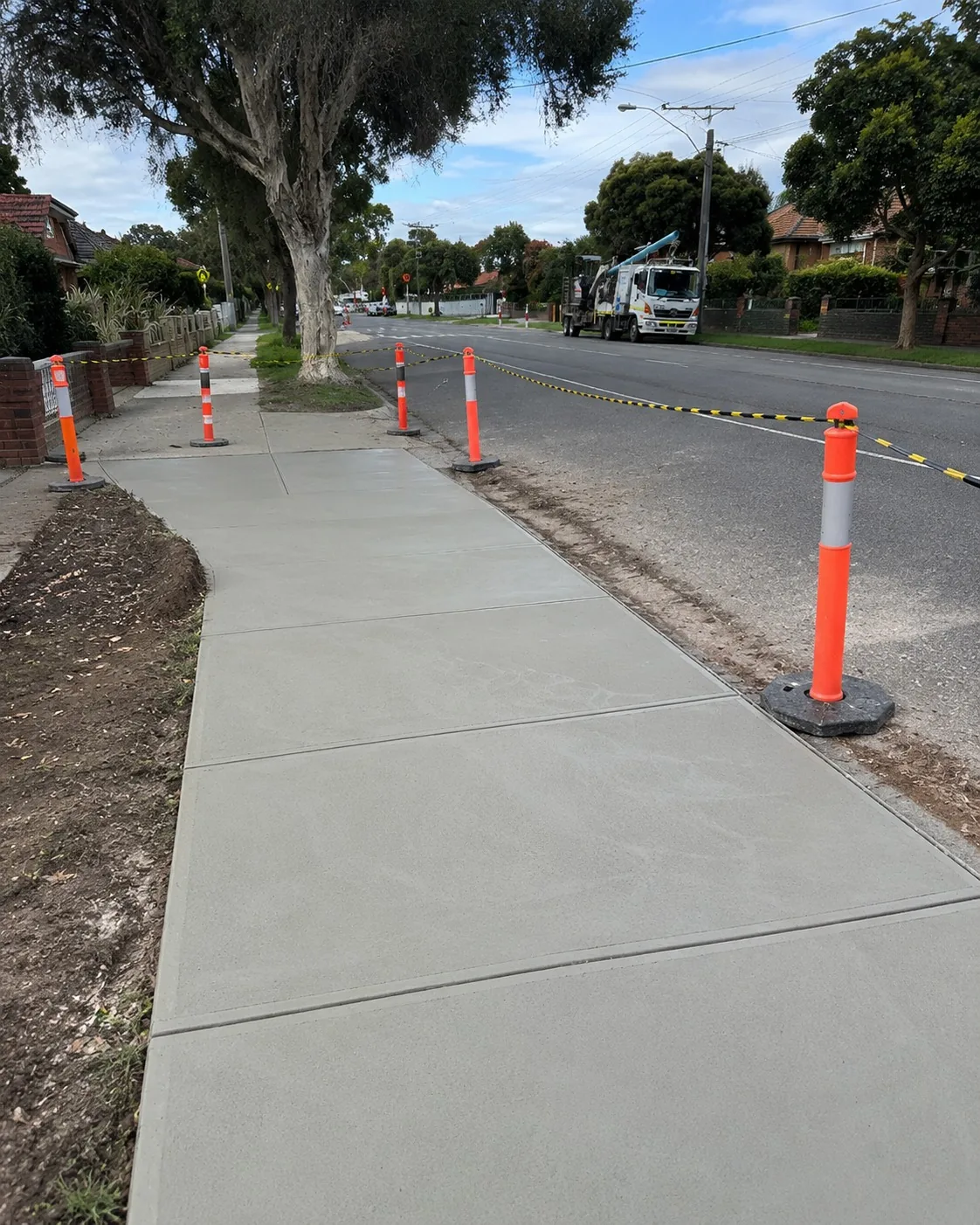 New concrete footpath running along a tree-lined Newcastle street behind bollards